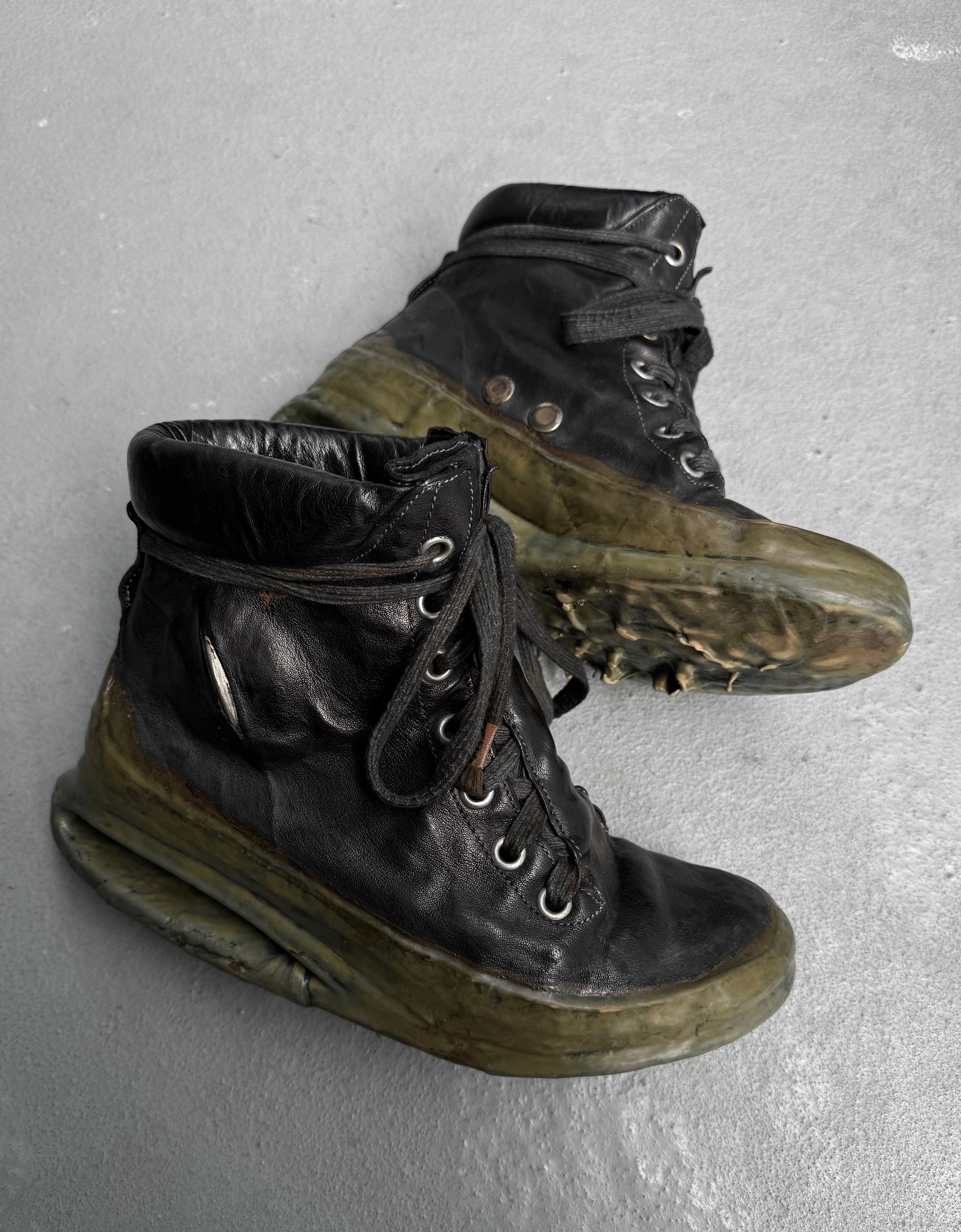 A pair of DRIEW Carol Christian Poell ‘AM/2685P ROOMS-PTC/12’ black high-top kangaroo leather sneakers (Size 6, EU 41.5-42) with thick translucent green soles, light wear, scuffs, creases, and loosely tied black laces rest on a gray surface.