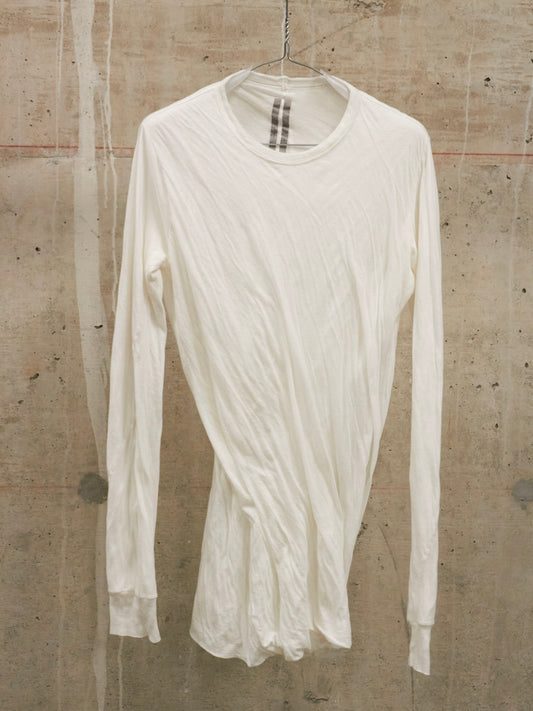 White long-sleeve shirt on a hanger against a textured wall.
