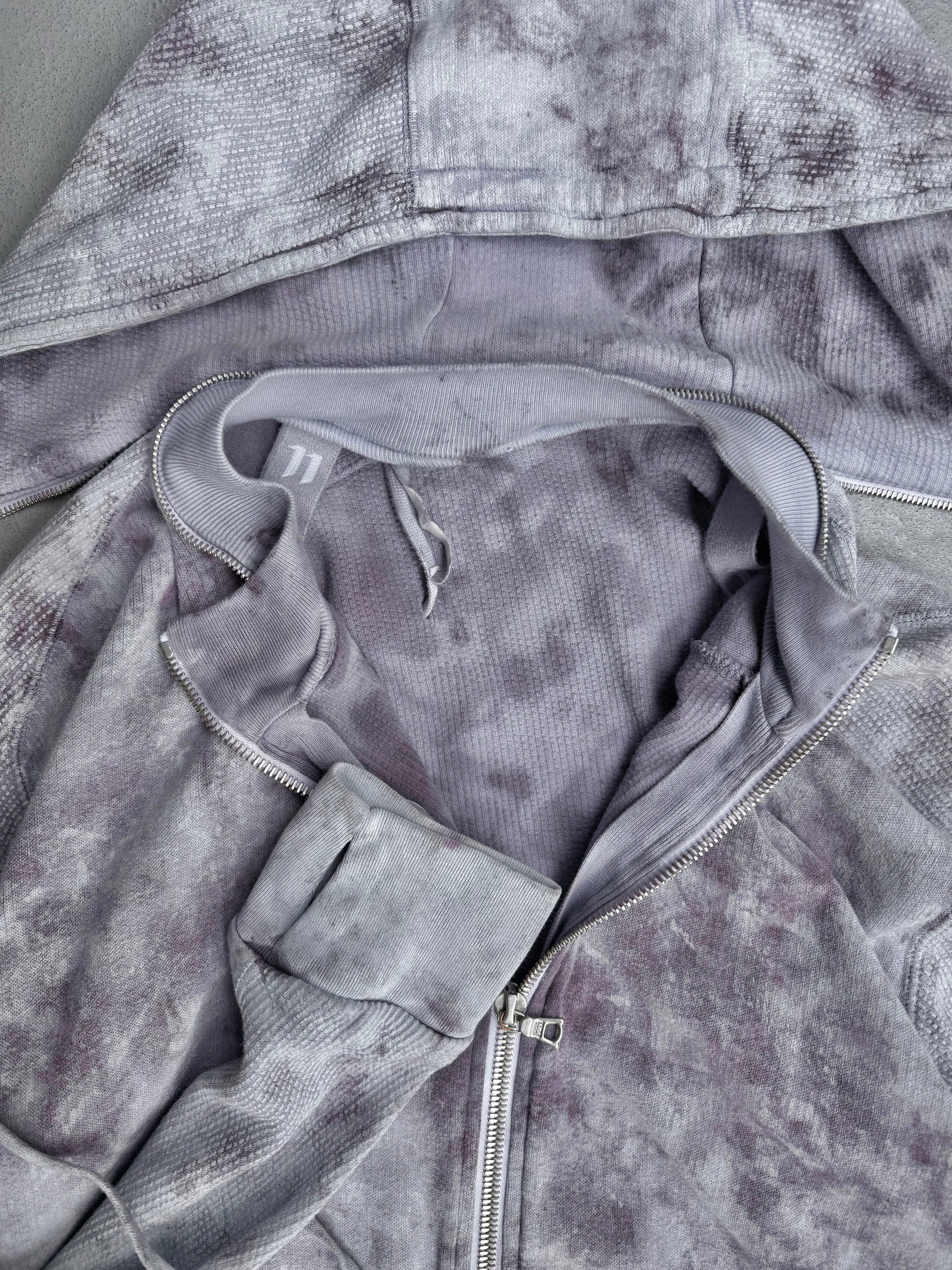 A close-up of the Boris Bidjan Saberi 11 SS23 ‘Z1-F1235’ Hand-dyed Convertible Hoodie in light purple and white, size XL, slim fit with hood and drawstrings, shown partially unzipped on a gray surface.