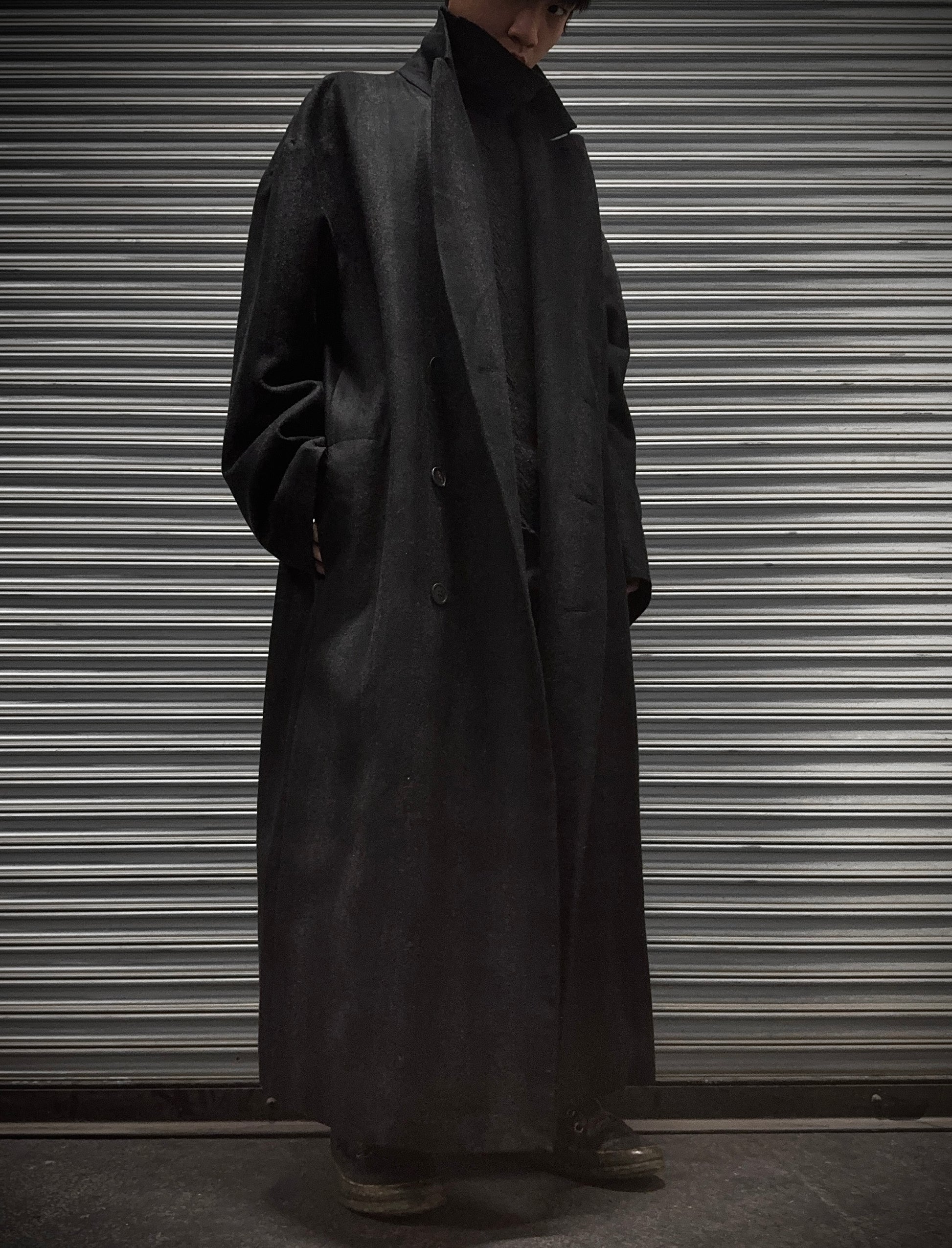 Person wearing a long dark coat standing in front of a metallic shutter.