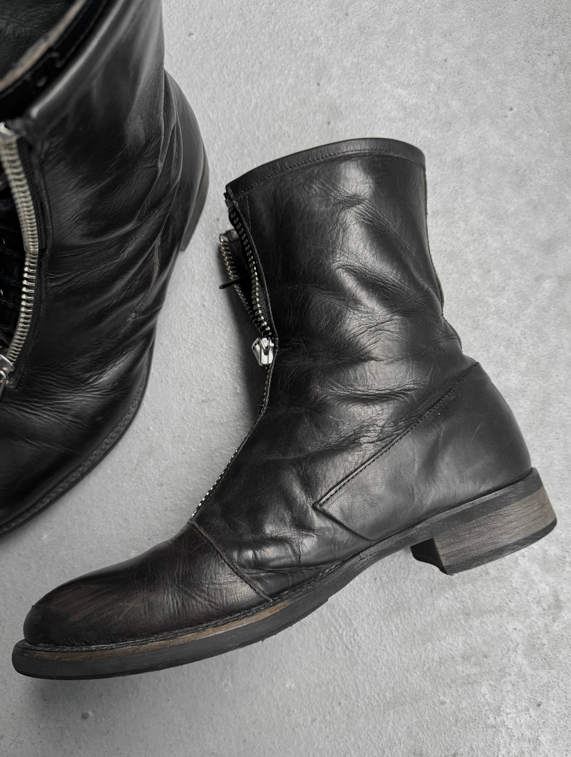 Black leather boots with zippers on a gray surface