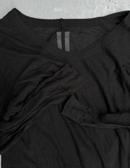The Rick Owens SS10 “RELEASE” Black Sheer Long-sleeves is laid flat on a gray surface, its long sleeves casually folded across the front, showcasing the brands signature contemporary style.