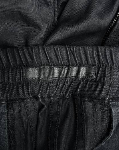 Close-up of the inside waistband of Julius_7 SS10 “neurbanvolker;” Convertible Multi-zip Cotton Twill Shorts by DRIEW in black, showing an empty black leather label, gathered fabric, visible stitching, part of a zipper, fits US 29-32 or size 2.
