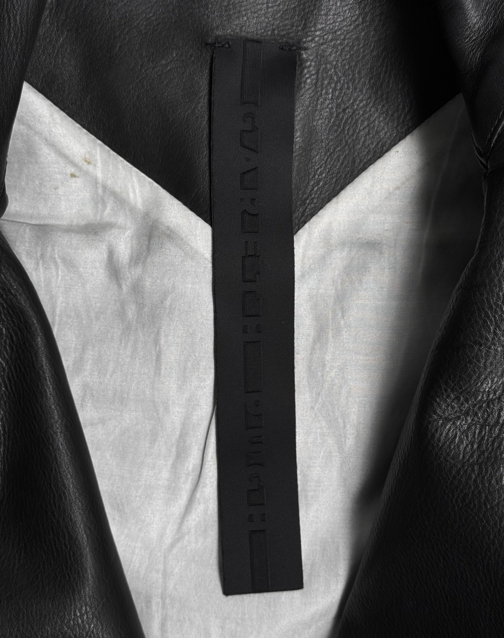 Close-up of the inside collar of a Gareth Pugh AW09 Detachable Sleeves Horse Leather Rider’s Jacket, showing a black tag with embossed, unreadable characters and a light gray inner lining.