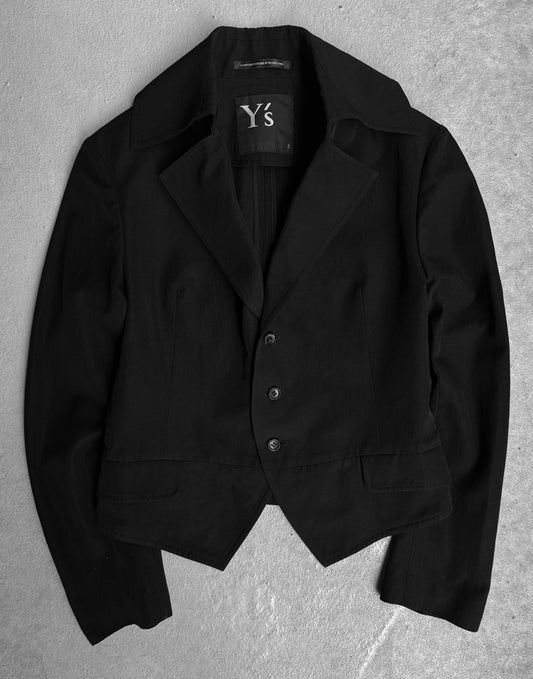 The Y’s by Yohji Yamamoto SS07 cropped cotton-blend blazer, featuring a black tailored fit with three buttons and notched lapels, is shown on a light gray textured surface, showcasing the refined Japanese designer style.