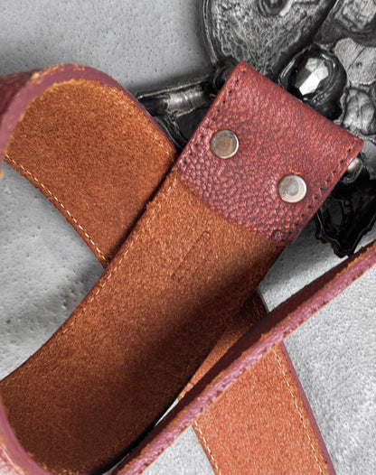 Close-up of a Tornado Mart Early 00s Pirate Silver Buckle Leather Belt in flawless brown leather with textured detail and two metal rivets, shown on gray next to an ornate silver piece. Fits US 32-36 Waist (Size M).