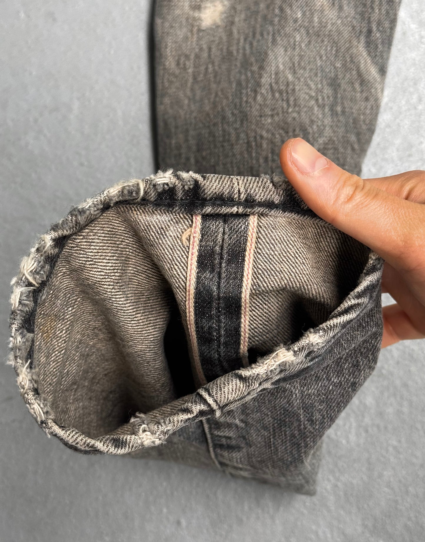 A hand folds the cuff of Mihara Yasuhiro AW10 Double-pockets Repair Patchwork Selvedge Denim, revealing a pink selvedge edge—classic streetwear with fraying details showing Mihara Yasuhiro’s signature craftsmanship.