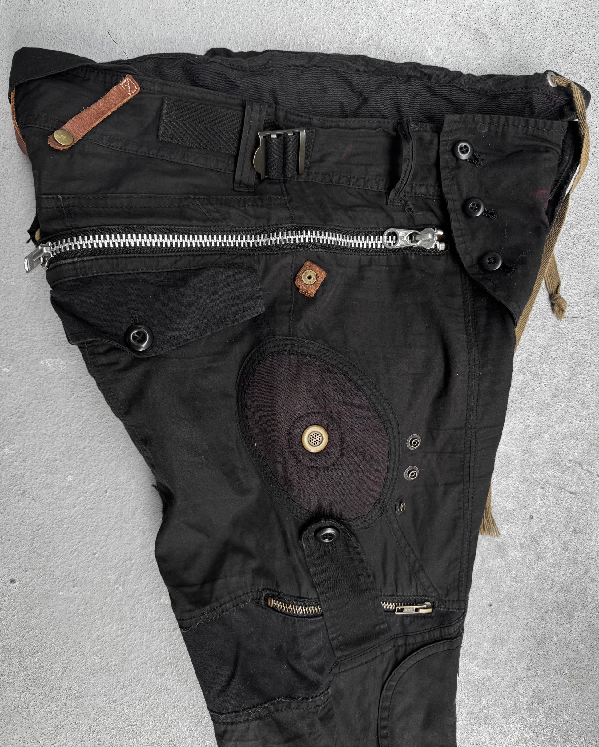 L.G.B Early 00s Pilot Cargo Capris by L.G.B, US 32 Waist, black with multiple zippers, buttons, repair patches, and pockets. Features an asymmetrical design and varied fabric textures. Minor staining visible. Laid flat on a gray surface.