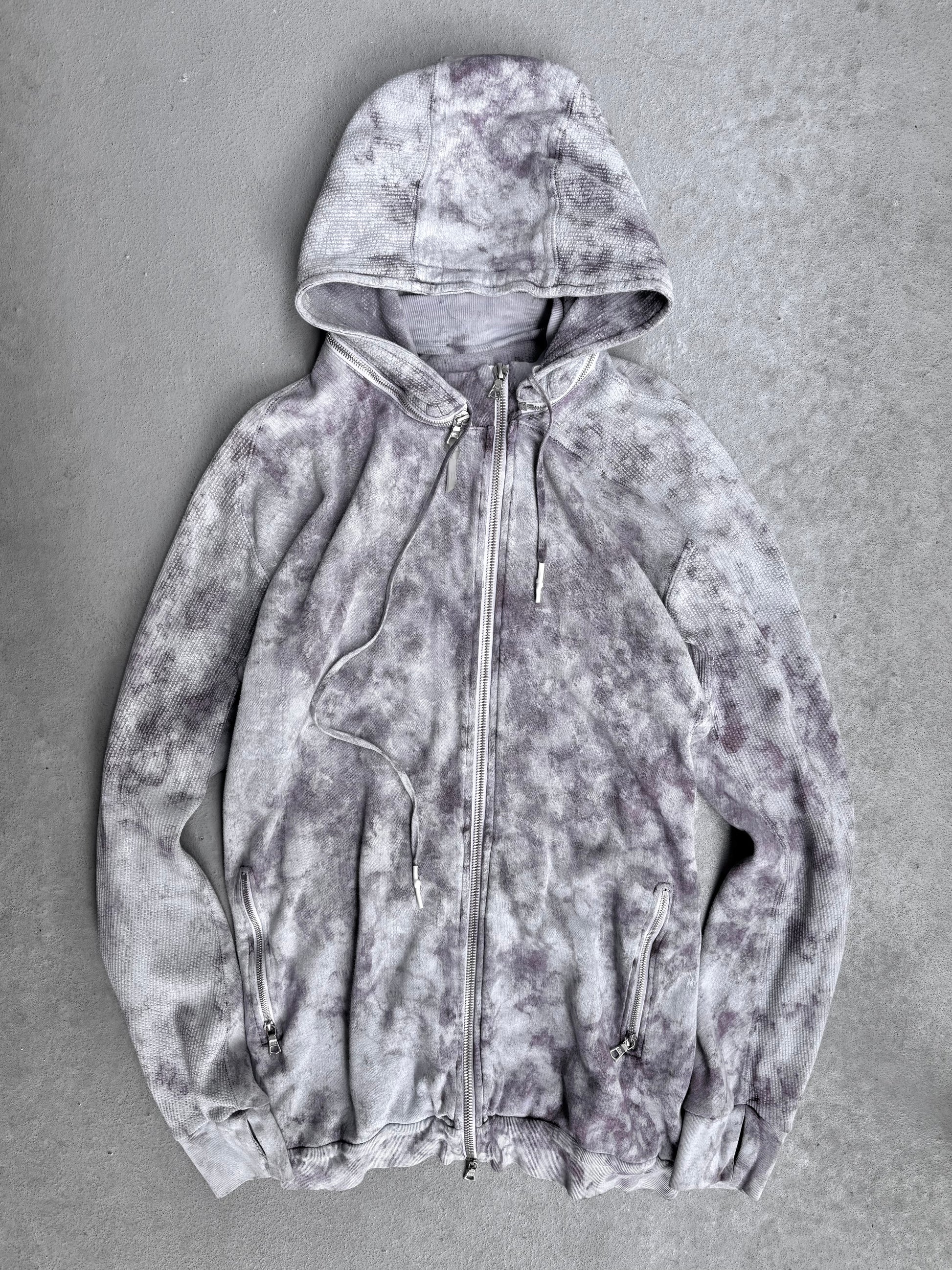 The 11 by Boris Bidjan Saberi SS23 ‘Z1-F1235’ Hand-dyed Convertible Hoodie features a light gray zip-up design with dark gray and purple tie-dye, hood, drawstrings, and front zip pockets—signature avant-garde style from Boris Bidjan Saberi.