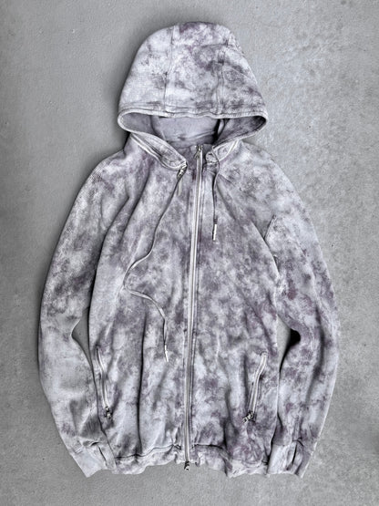 The 11 by Boris Bidjan Saberi SS23 ‘Z1-F1235’ Hand-dyed Convertible Hoodie features a light gray zip-up design with dark gray and purple tie-dye, hood, drawstrings, and front zip pockets—signature avant-garde style from Boris Bidjan Saberi.