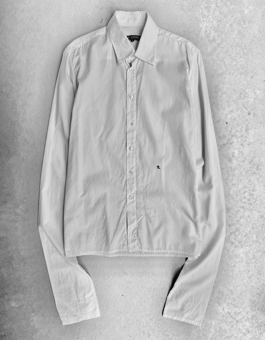 The RAF SIMONS AW05-06 “History Of My World” Extended Sleeves Button-up Shirt is laid flat on a textured light surface, collar up and cuffs bent, showcasing the brands contemporary style and subtle avant-garde design.