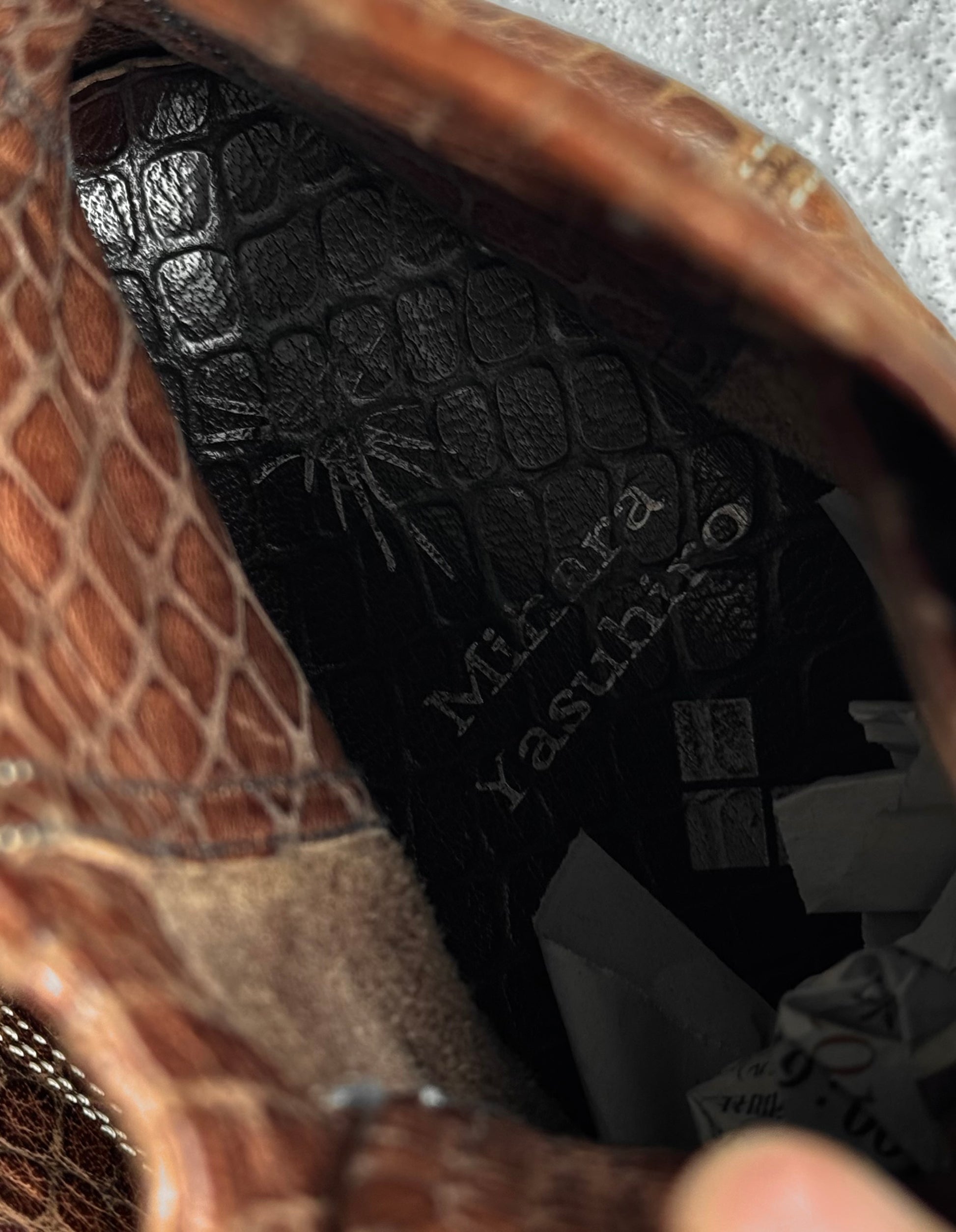 Close-up of Mihara Yasuhiro Early 00s Python Embossed Cow Leather Pointy Toe Boots’ brown textured leather, highlighting the “Minerva yasubira” embossing inside—a detail reflecting Mihara Yasuhiro’s unique avant-garde style.