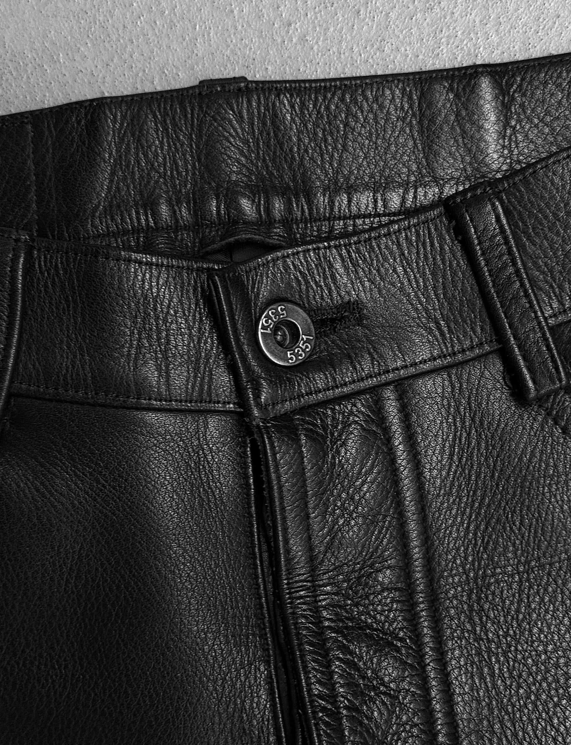 Close-up of black leather pants with a button detail on a light gray background