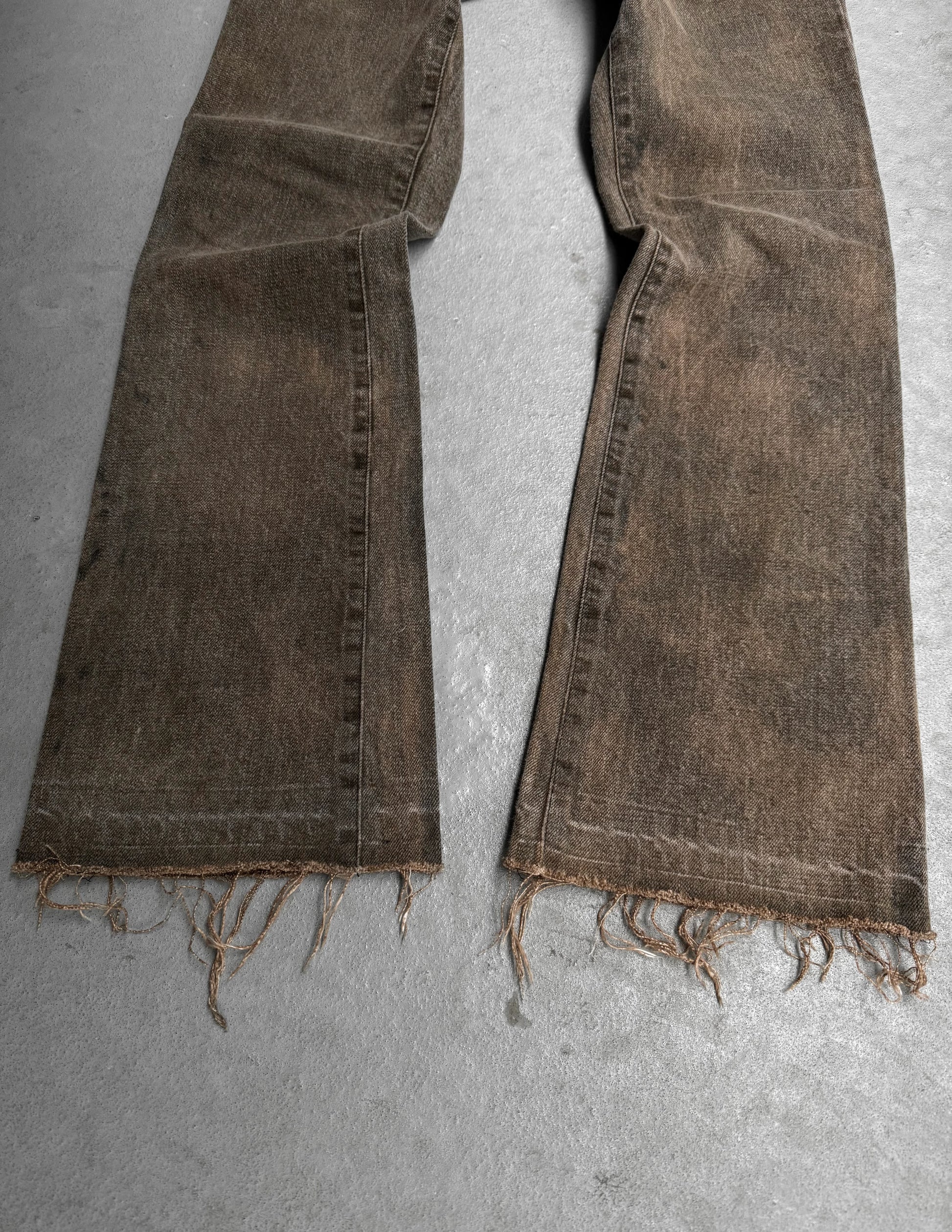 Brown distressed jeans laid flat on a gray surface