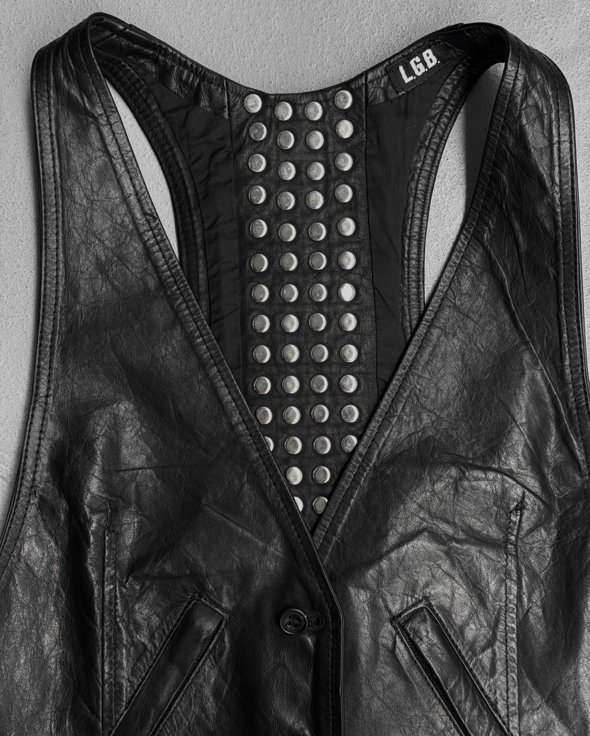 The L.G.B Early 00s Calfskin Leather Studded Mini-vest features black leather, a deep V-neck, studded back detailing, two front pockets, and a visible inner collar label for signature Japanese style.