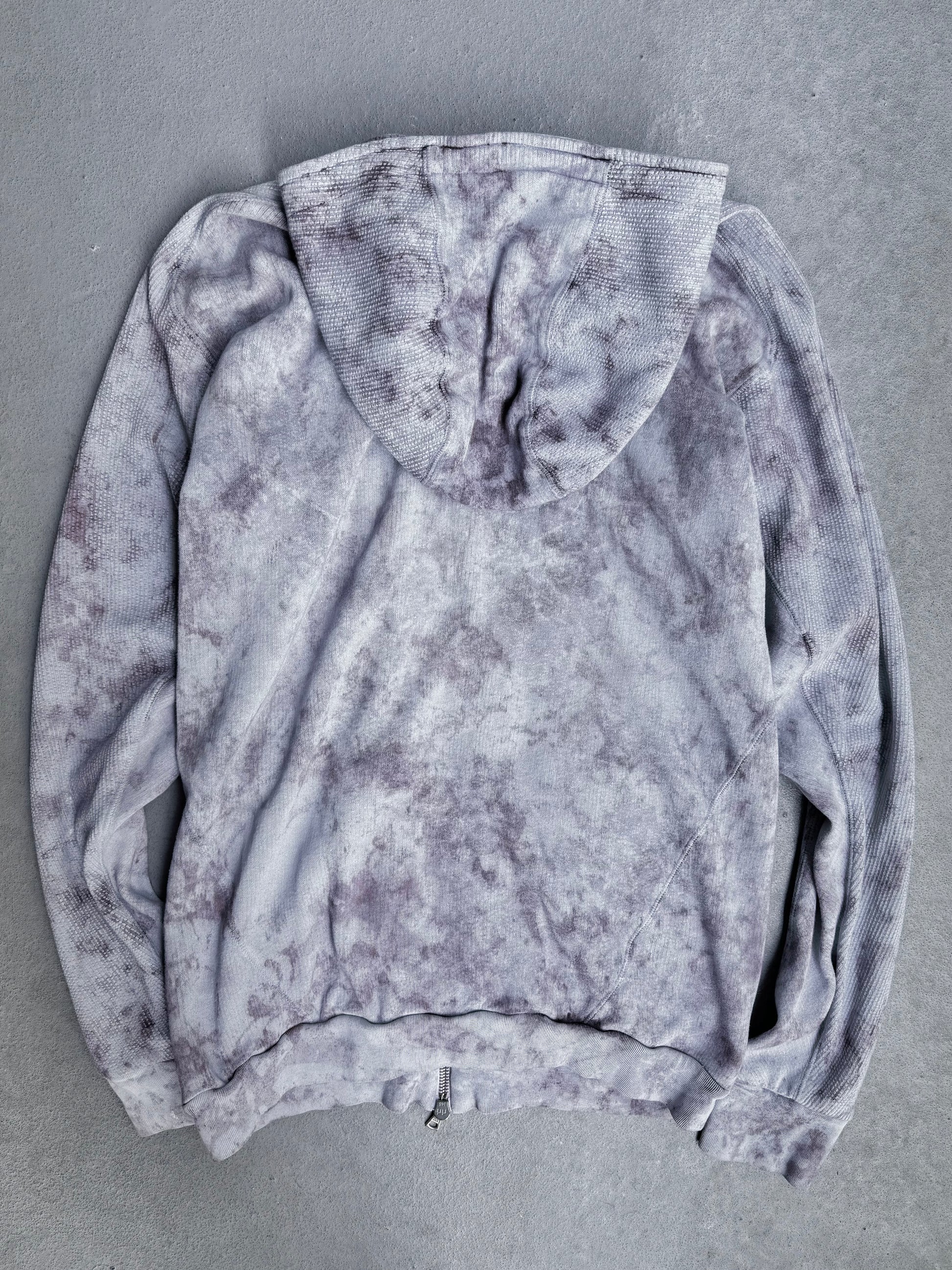 The Boris Bidjan Saberi 11 SS23 ‘Z1-F1235’ Hand-dyed Convertible Hoodie in Size XL, shown from the back on a light gray surface, features a light gray and purple tie-dye design with visible sleeves and hood, offering a slim modern fit.