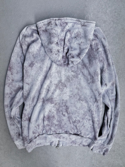 The Boris Bidjan Saberi 11 SS23 ‘Z1-F1235’ Hand-dyed Convertible Hoodie in Size XL, shown from the back on a light gray surface, features a light gray and purple tie-dye design with visible sleeves and hood, offering a slim modern fit.