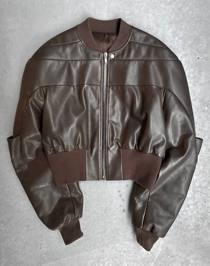 The Rick Owens AW23 LUXOR Girdered Leather Bomber Jacket, in cropped brown calfskin with a front zipper and ribbed collar, cuffs, and waistband, is shown laid flat on a gray surface.