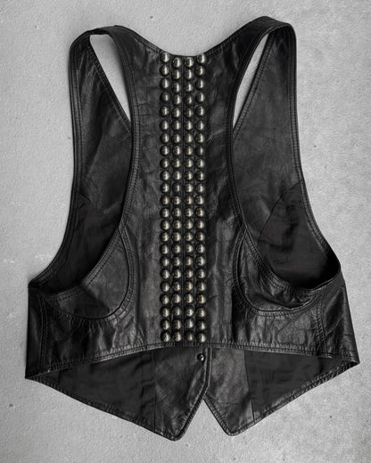 The L.G.B Early 00s Calfskin Leather Studded Mini-vest by L.G.B is a black racerback vest with two vertical rows of large metallic studs down the back, inspired by Japanese fashion and shown on a light gray surface.