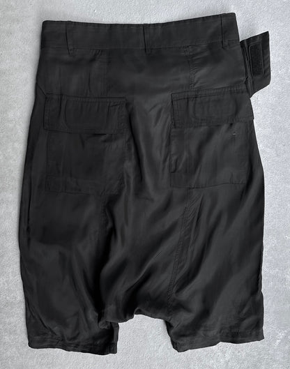 The Rick Owens SS14 “VICIOUS” Lightweight Memphis Shorts, in black, feature two large back flap pockets, an adjustable waistband strap, and a slightly wrinkled texture, shown laid flat on a light gray surface.