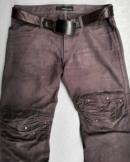 ANDREW MACKENZIE Early 00s Stud Darted Knee Denim: Distressed dark brown jeans with large knee rips, folded knee detailing, and metal rivets, shown flat with a worn leather belt.
