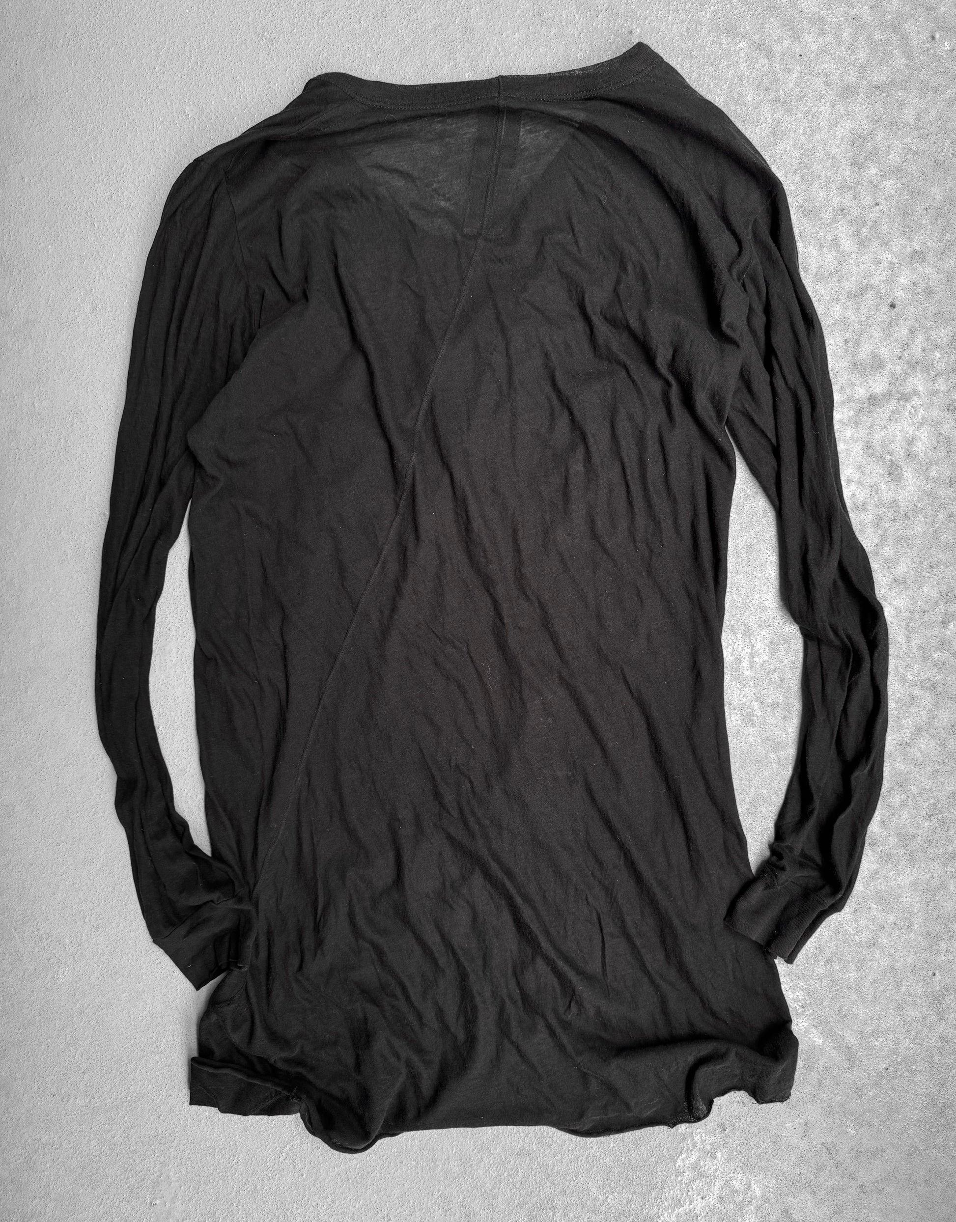 The Rick Owens SS10 “RELEASE” black sheer long-sleeve shirt lies flat and inside-out on a light gray textured surface, its wrinkled, semi-transparent fabric evoking the edgy, avant-garde style iconic to Rick Owens.