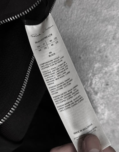 A hand holds a white label with black text showing fabric details, care instructions, size, and MADE IN MOLDOVA on a Rick Owens SS24 “LIDO” Nubuck Leather Cropped Flight Bomber Jacket near a black zipper against a grey background.