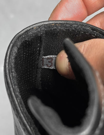 A close-up of a hand holding open the tongue of a new Carol Christian Poell ‘AM/2759SP-IN CORSS-PTC’ Kangaroo Leather Buckle Drip Boot, revealing a fabric tag with the number 13.