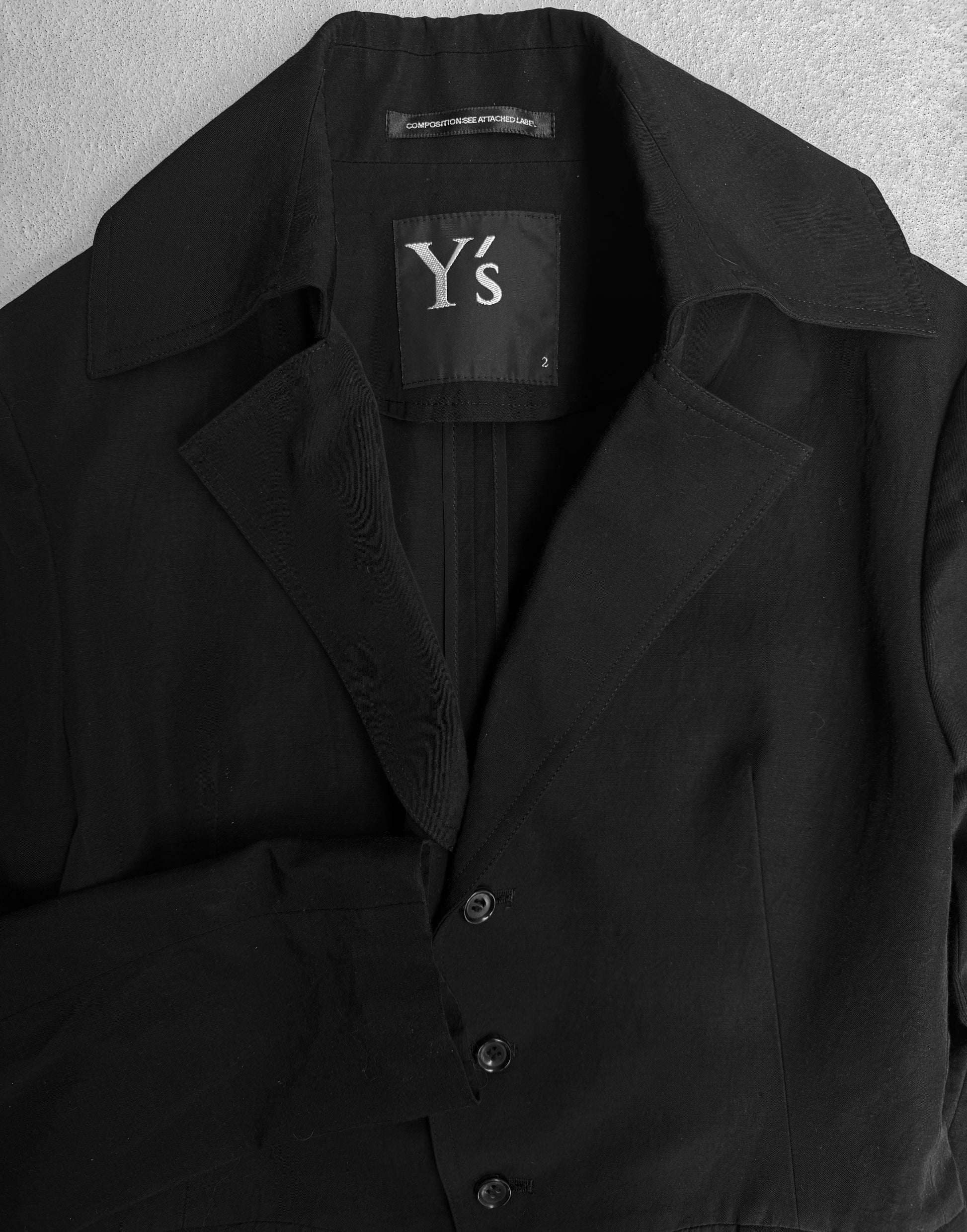The Y’s by Yohji Yamamoto SS07 Cropped Cotton-blend Blazer features wide lapels, three buttons, and a bold Y’s label inside—a standout piece of Japanese designer fashion by Yohji Yamamoto, shown laid flat on a light surface.