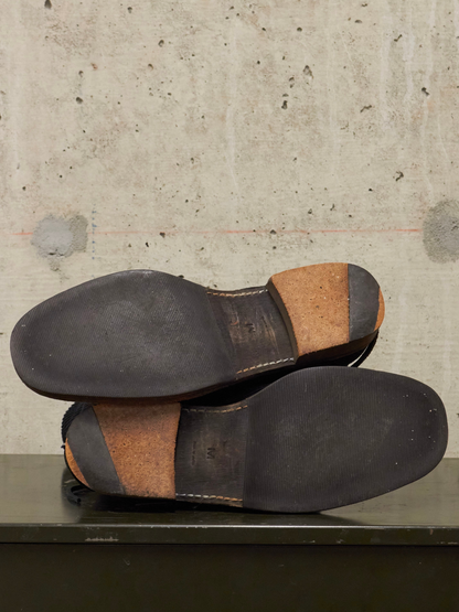 Pair of black leather shoes with brown soles on a concrete surface