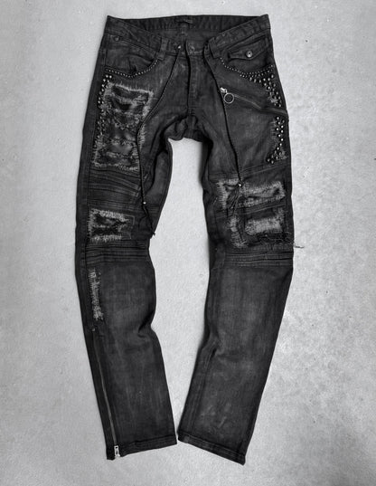 KMRii Early 00s Goatskin Patches Studded Crush Flare-zip Denim in black, US 29-30 waist. Features multiple rips, patches, studs, zippers, and metal ring details with slight fading for an edgy look. Laid flat on a light surface.