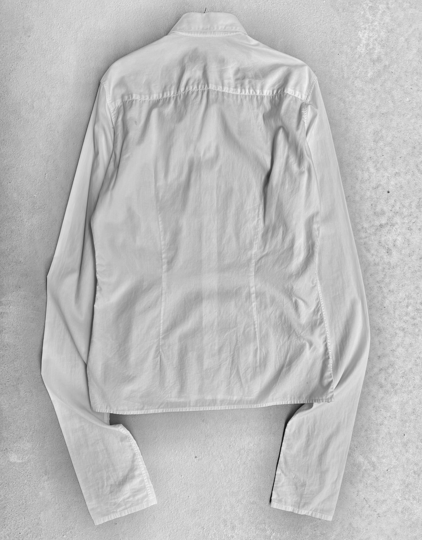 The RAF SIMONS AW05-06 History Of My World Extended Sleeves Button-up Shirt is shown laid flat, back side up, highlighting its light color, collar, and long sleeves. The shirt has a contemporary design and appears slightly wrinkled.