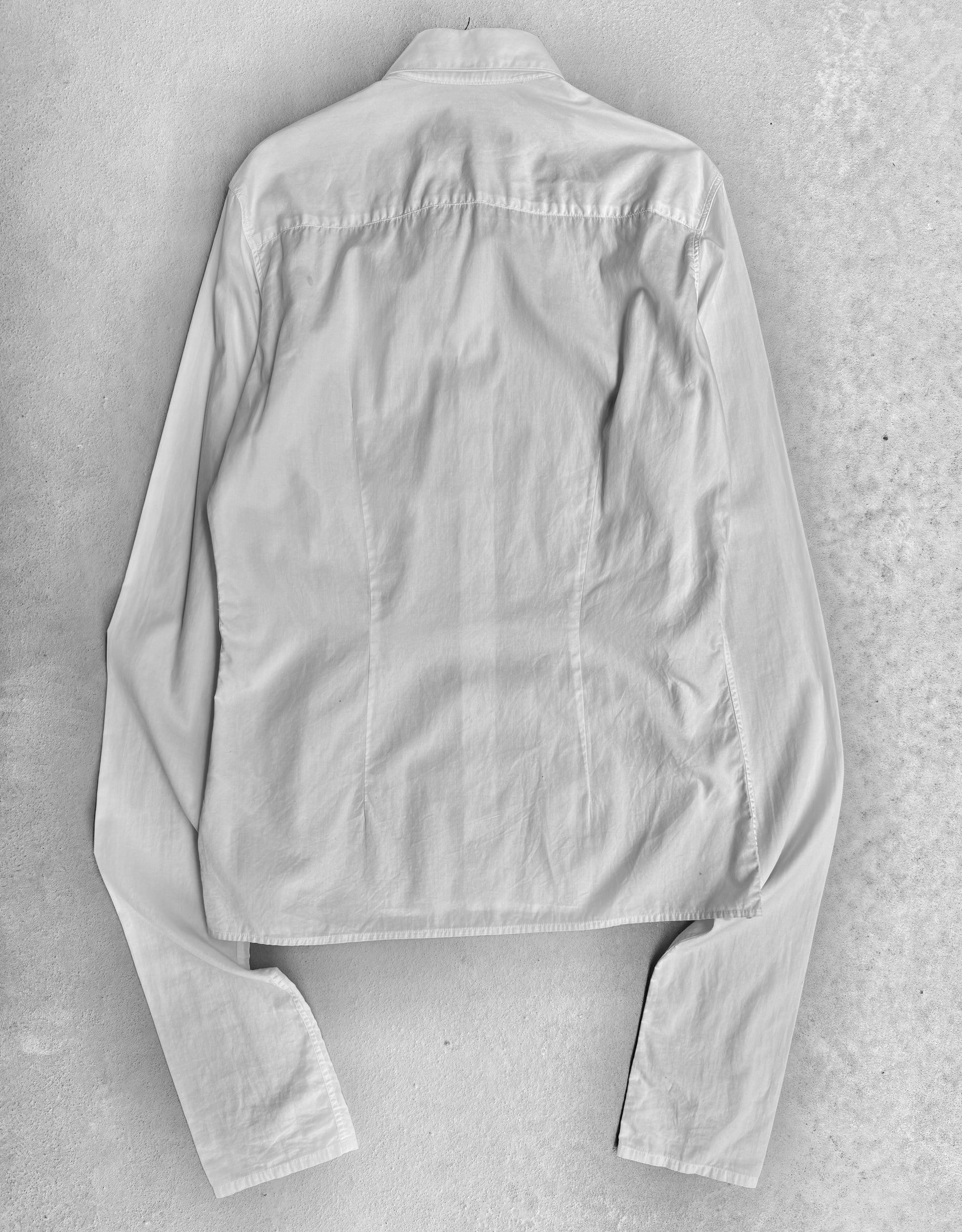 The RAF SIMONS AW05-06 History Of My World Extended Sleeves Button-up Shirt is shown laid flat, back side up, highlighting its light color, collar, and long sleeves. The shirt has a contemporary design and appears slightly wrinkled.