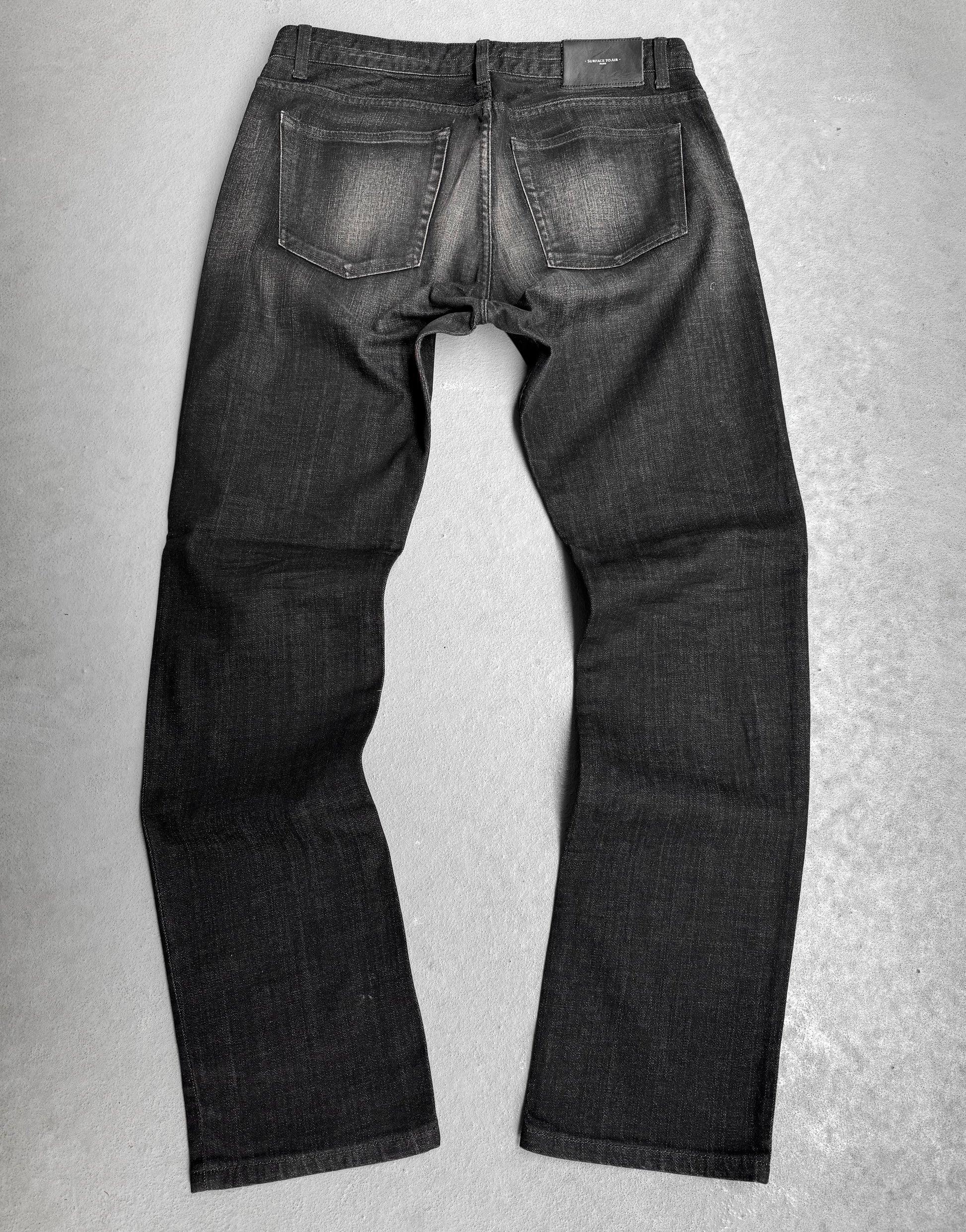 The Surface To Air SS14 Faded Black Bootcut Skinny Denim is displayed flat on a grey surface, showcasing the back with visible pockets and subtle seam fading—ideal for those who value urban style in modern menswear.