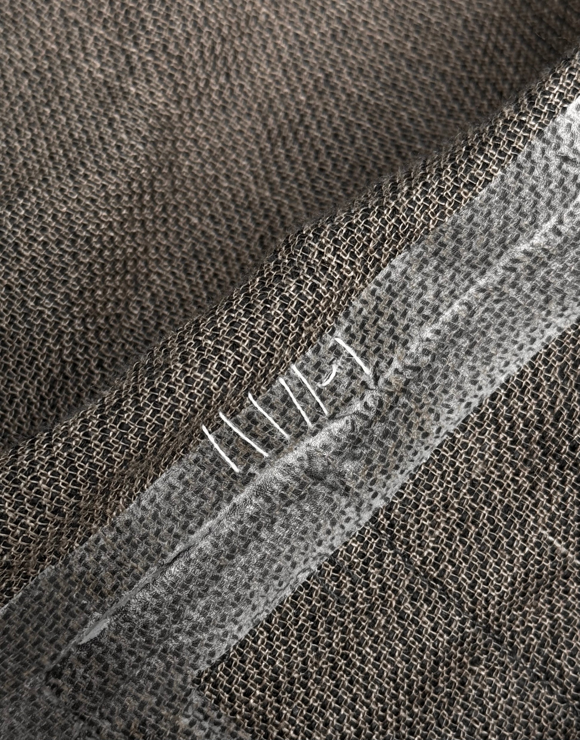 Close-up of brown burlap fabric from the TaichiMurakami “Coin” Taped Seam Collarless Work Blazer, featuring a reinforced seam with white hand stitching and translucent tape, reflecting the brand’s signature industrial minimalism.