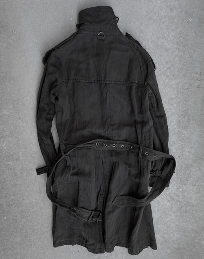 The ATTACHMENT by Kazuyuki Kumagai Raglan Doctor Trench Coat is laid flat on a gray concrete surface, displaying its back and sleeves—a sleek piece from Attachment by Kazuyuki Kumagai.