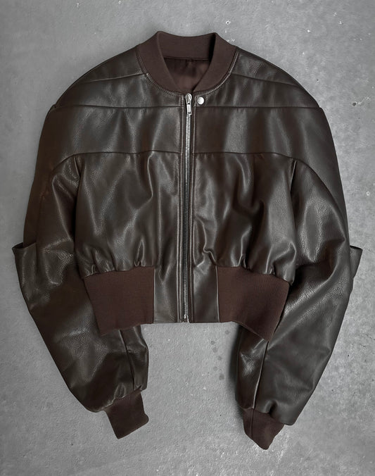 The Rick Owens AW23 LUXOR Girdered Leather Bomber Jacket, in dark brown with ribbed cuffs, collar, and waistband, features a front zipper and glossy finish for a high-fashion look with gothic grunge flair, displayed on a gray surface.