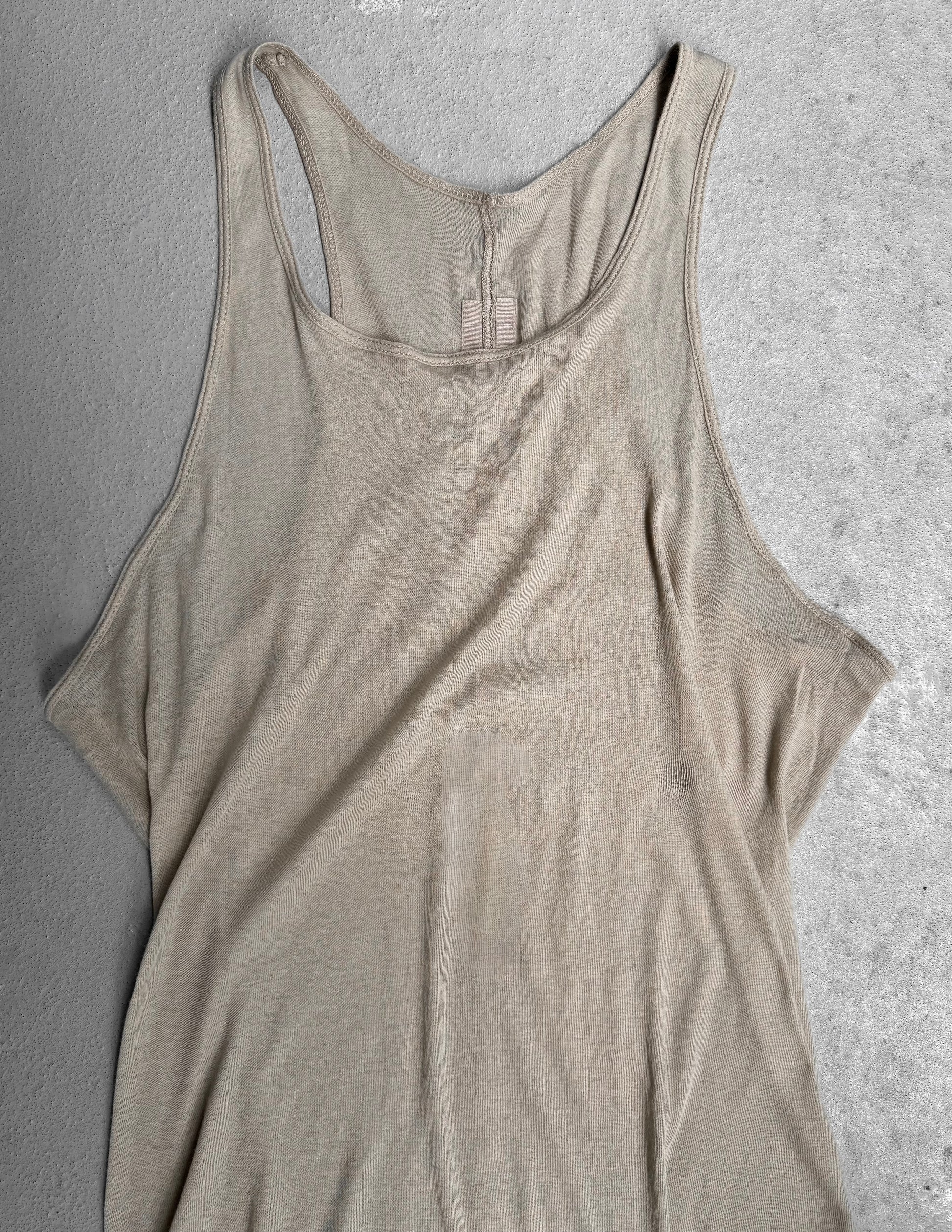 The Rick Owens SS24 “LIDO” Pearl Sheer D-Flap Tank Top, a beige sleeveless racerback style, is laid flat on a light gray textured surface.