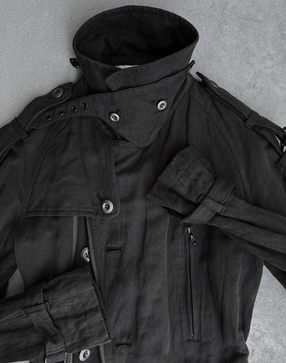 A dark grey ATTACHMENT by Kazuyuki Kumagai Raglan Doctor Trench Coat with a high collar, multiple buttons, epaulets, strap details, and a zippered pocket lies flat on a light grey surface—a refined menswear piece.