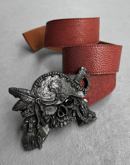 The Tornado Mart Early 00s Pirate Silver Buckle Leather Belt, inspired by Japanese men’s fashion, features a brown leather strap and a detailed pirate skull buckle with a tricorn hat, feathers, and eye patch, shown on a light gray surface.