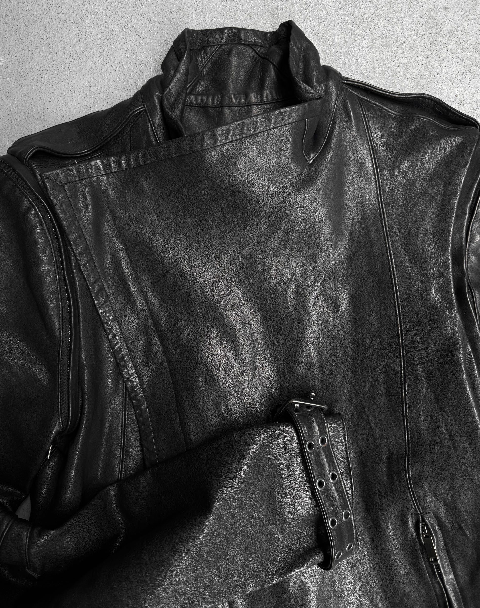The Gareth Pugh AW09 Detachable Sleeves Horse Leather Riders Jacket, featuring an asymmetrical front zipper, shoulder epaulets, and a belted waist, is showcased laid flat on a light grey surface.