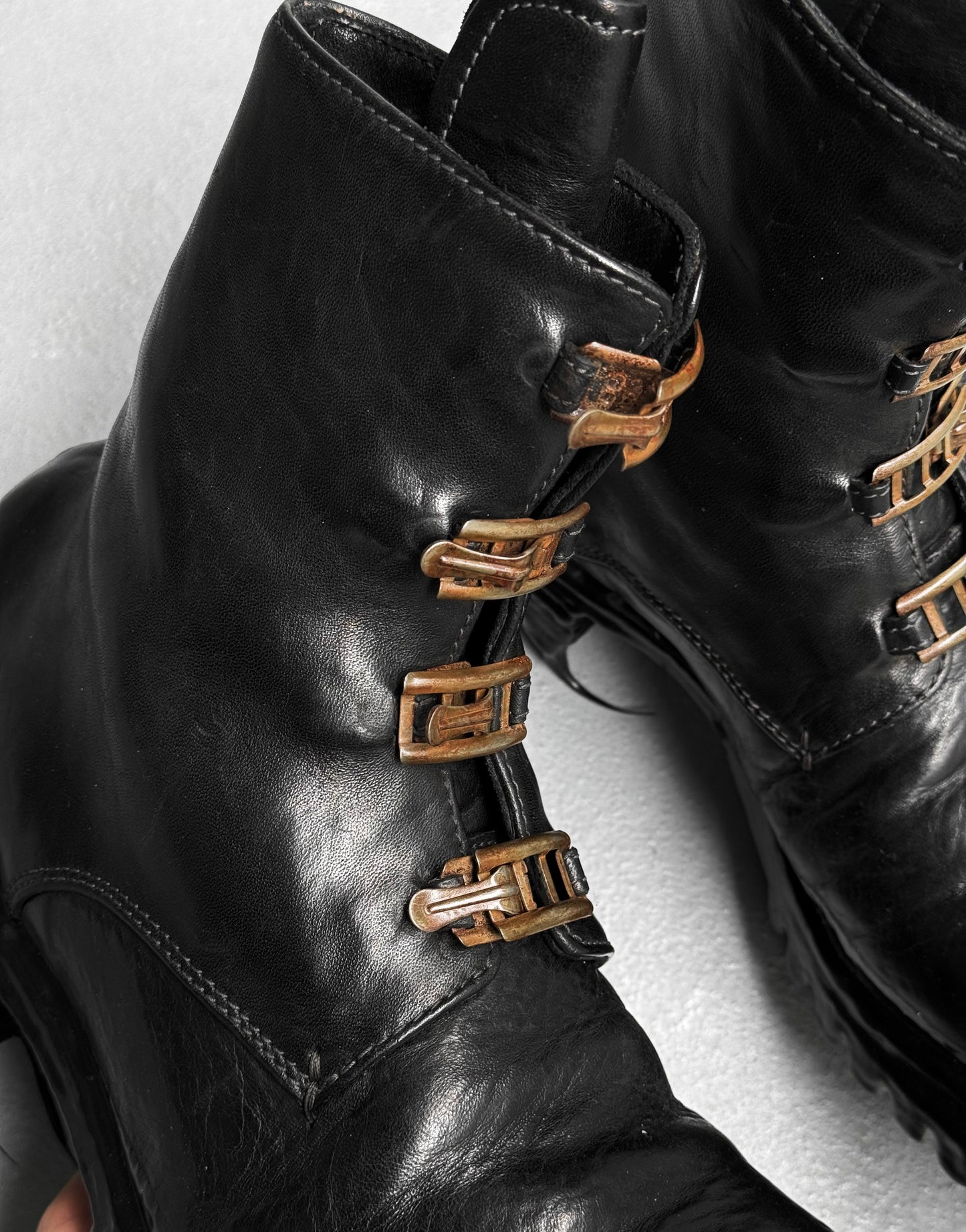 Close-up of Carol Christian Poell ‘AM/2759SP-IN CORSS-PTC’ Horse Leather Buckle Drip Boots in black, featuring worn brass-toned buckles, detailed stitching, and a rugged texture.