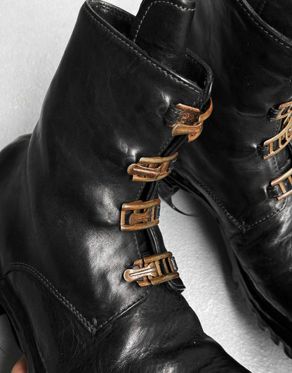 Close-up of Carol Christian Poell ‘AM/2759SP-IN CORSS-PTC’ Horse Leather Buckle Drip Boots in black, featuring worn brass-toned buckles, detailed stitching, and a rugged texture.