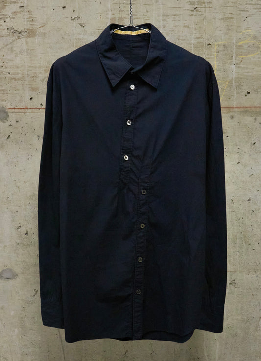 A dark navy blue long-sleeve button-up shirt hanging on a wooden hanger against a textured concrete wall.