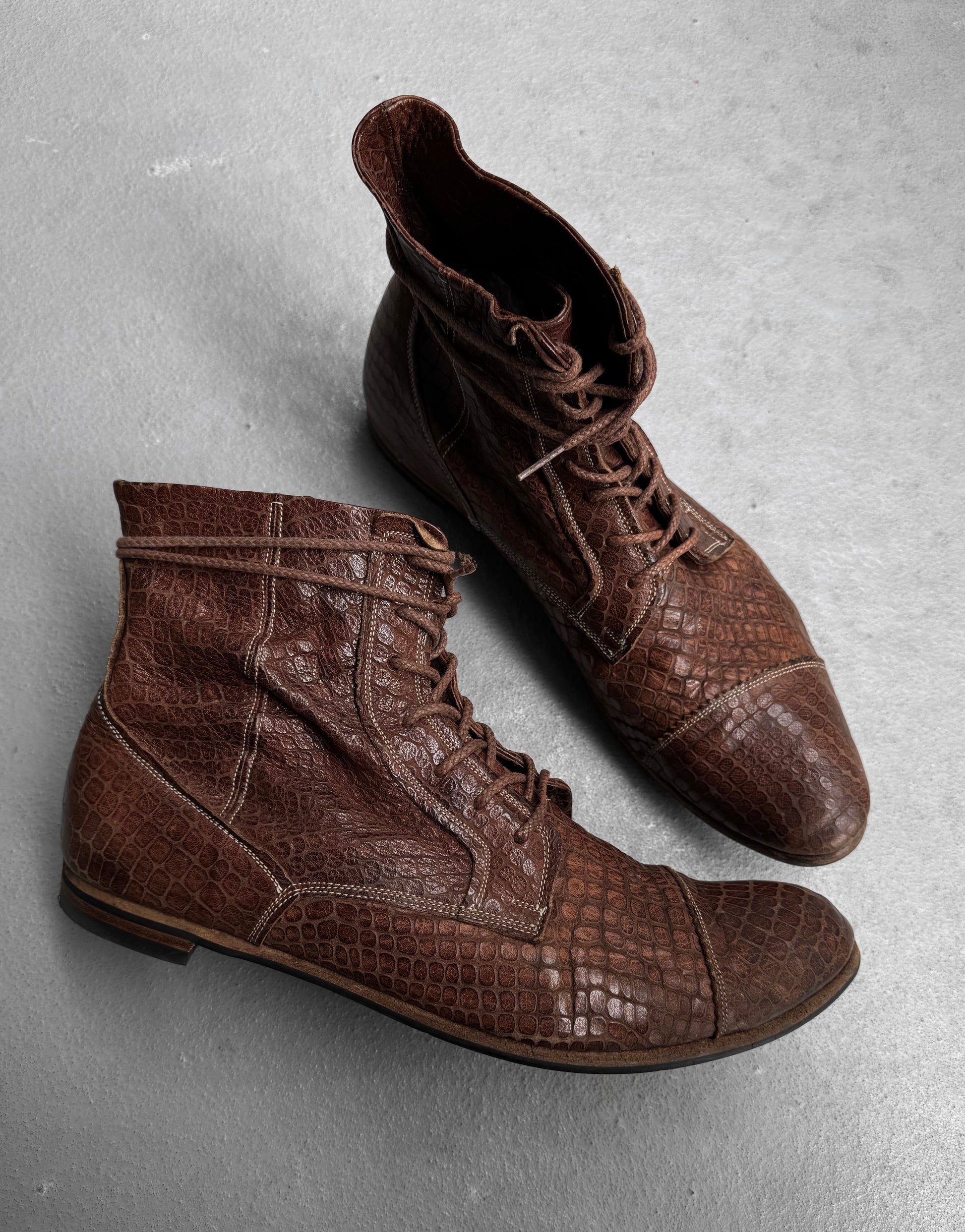 A pair of Mihara Yasuhiro Early 00s Python Embossed Cow Leather Pointy Toe Boots, featuring a textured, reptile pattern, are displayed on a light gray surface.