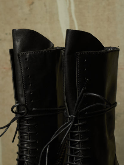 A close-up of a pair of black leather lace-up boots with pointed toes, set against a textured beige background.
