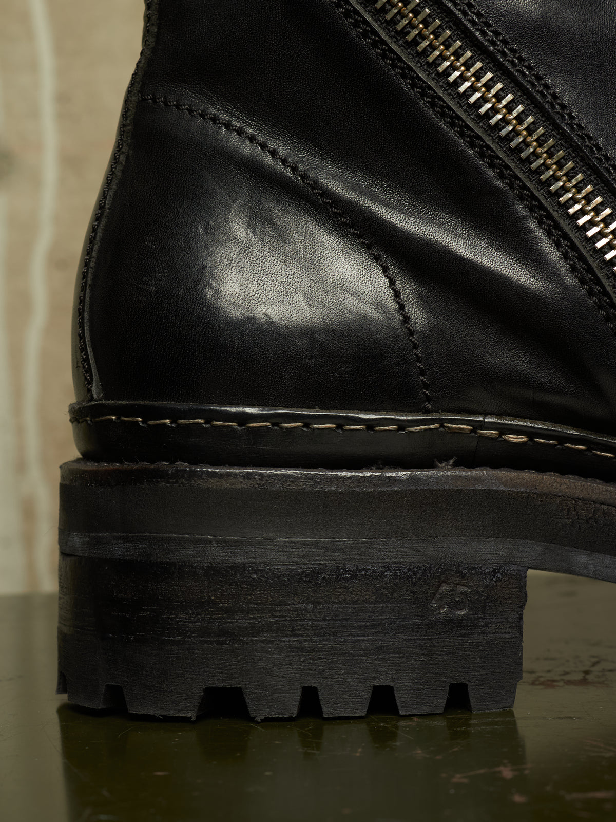 Close-up detail of a black leather ankle boot showing the side zipper, stitching, sole, and rugged lug outsole.