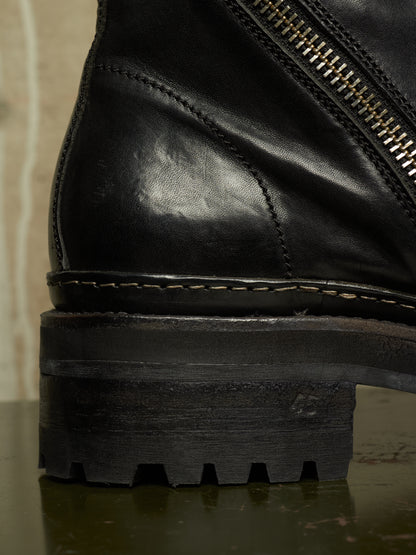 Close-up detail of a black leather ankle boot showing the side zipper, stitching, sole, and rugged lug outsole.