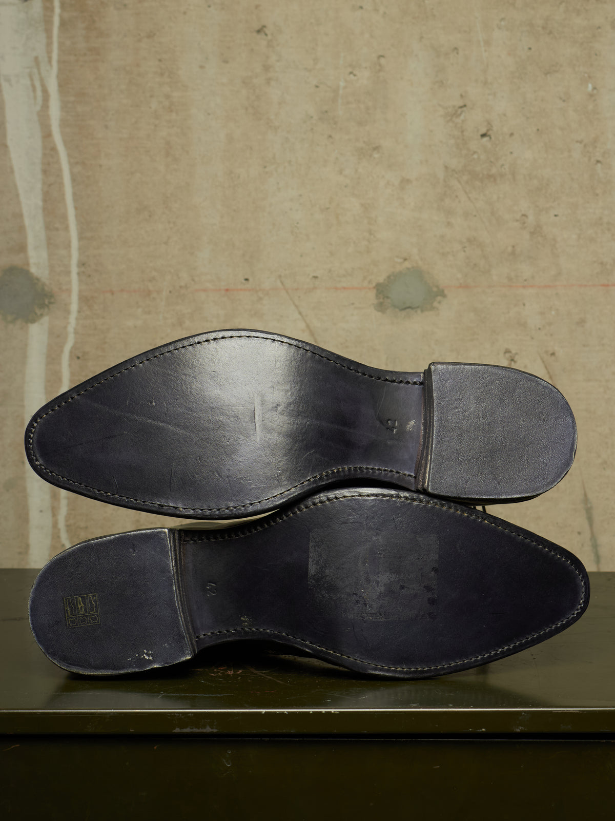 The soles of a pair of dark navy leather dress shoes, displayed flat against a textured beige background.