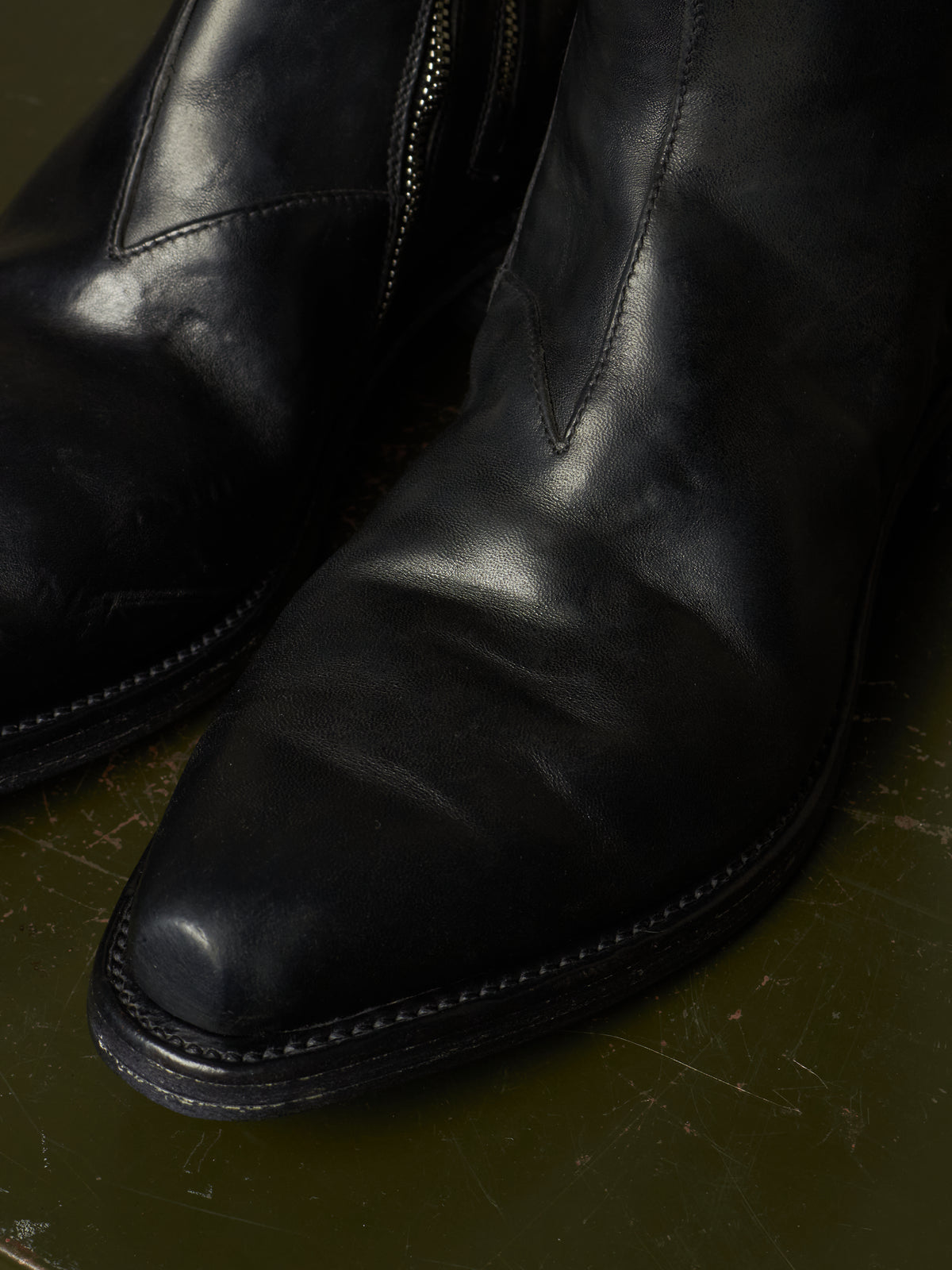 A close-up shot of a pair of black leather boots, showing the pointed toe, side zipper, and textured leather surface.